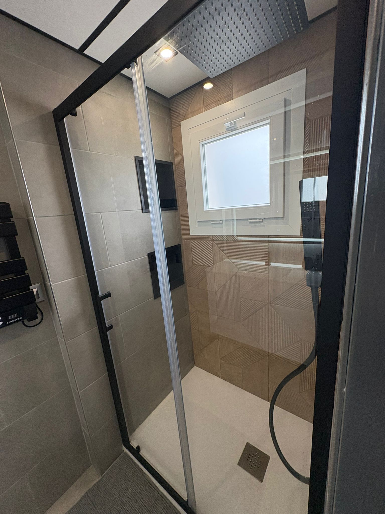 Eine moderne Dusche mit Glastüren, einer sichtbaren Bedienkonsole und einer gefliesten Wand.