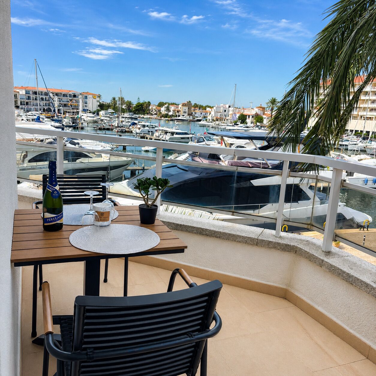 Un balcon donnant sur un port de plaisance, une bouteille de vin, un verre et une petite plante en pot.