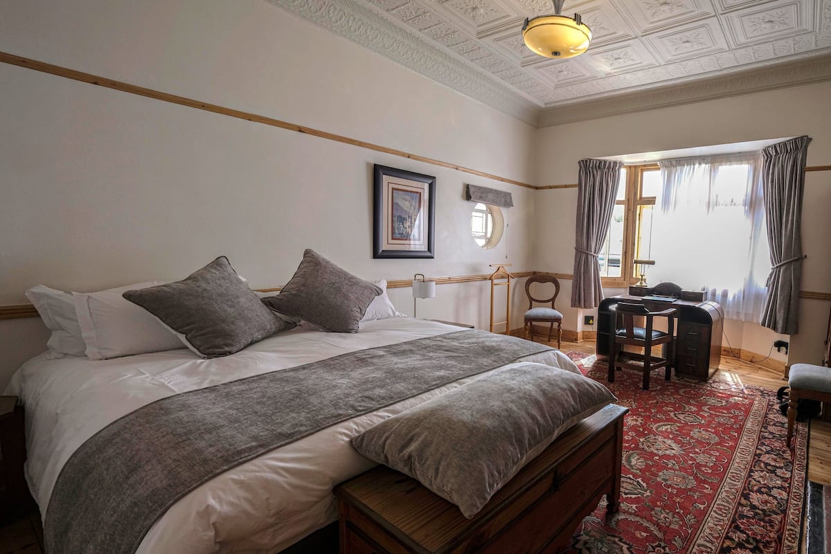 A bedroom with a large bed, a wooden bench, a desk, and a chair.