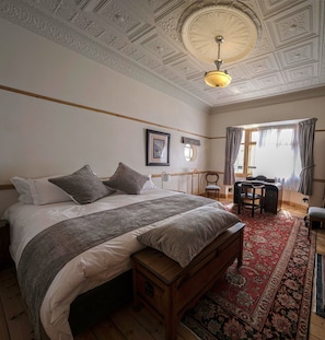 A bedroom with a large bed, a wooden bench, a desk, and a chair.