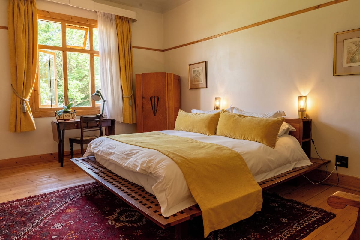 A bedroom with a wooden bed, a desk, a wardrobe, and a window with curtains.