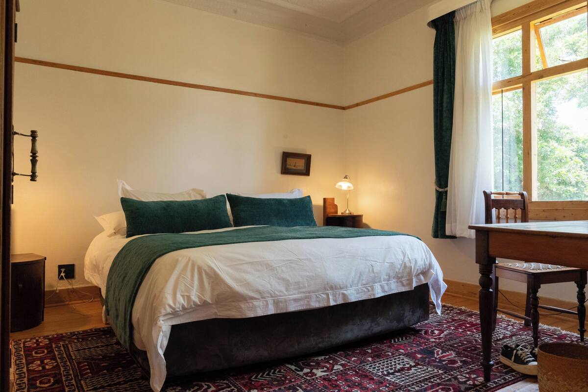 A bedroom with a bed, a nightstand, a lamp, a chair, and a window with curtains.