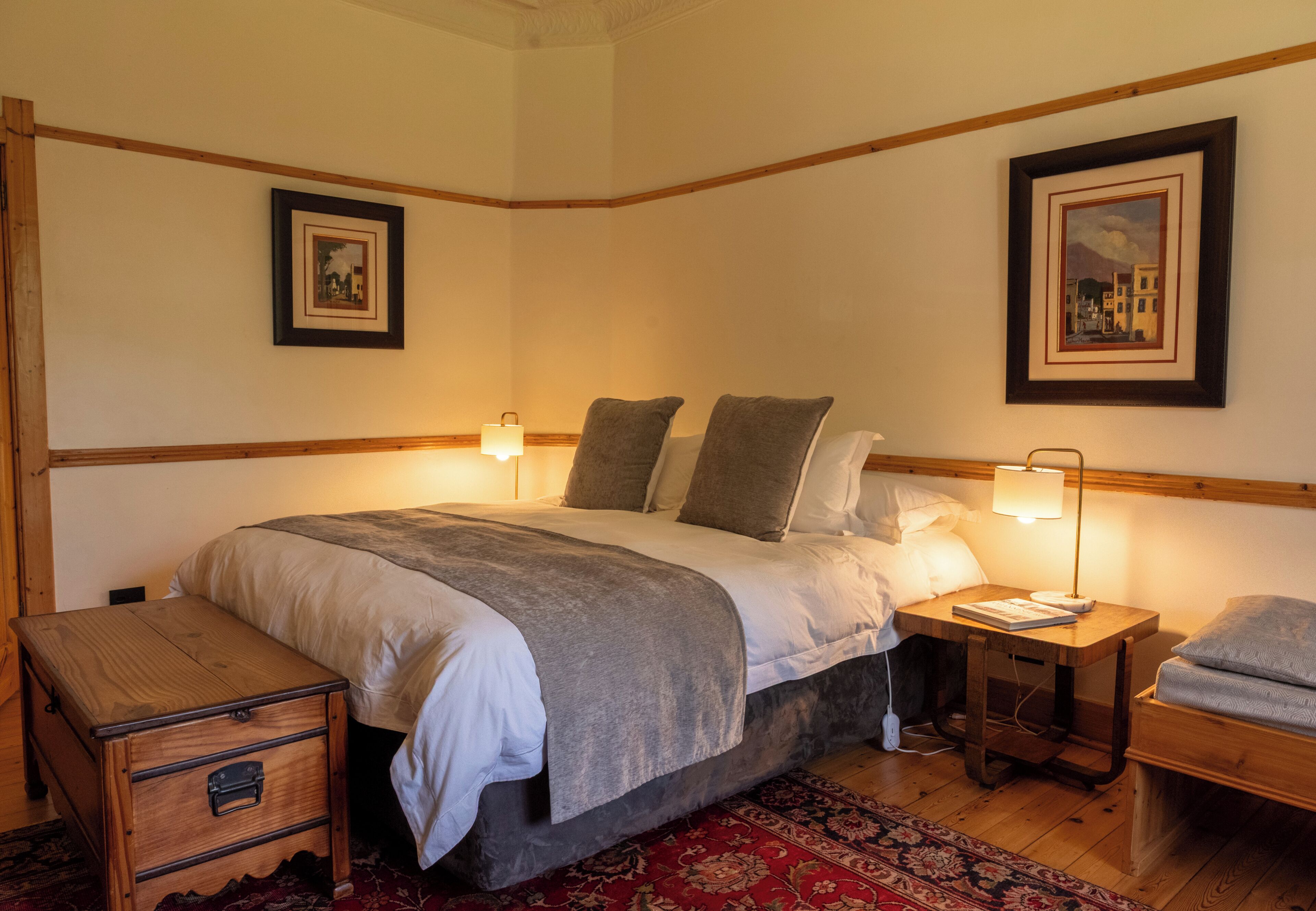 Een slaapkamer met een groot bed, nachtkastjes, een houten nachtkastje, een kast en twee ingelijste foto's aan de muur.