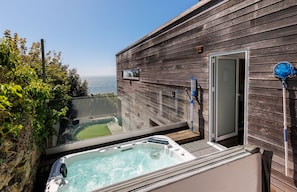 Eine Holzterrasse mit Whirlpool, Glasumrandung und Blick auf den Ozean.