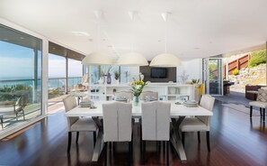 A modern dining area with a large table, four chairs, and a view of the ocean. - Kittiwake (Ventnor)