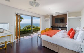 A modern bedroom with a large bed, a TV, and a view of the ocean. - Kittiwake (Ventnor)
