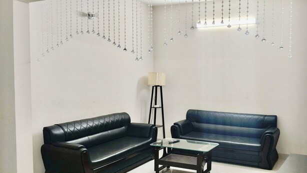 A living room with two black leather sofas, a glass coffee table, a floor lamp, and a chandelier.