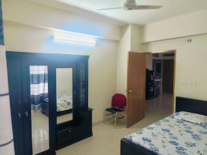 Un dormitorio con cama, armario, una silla y puerta que da a otra habitación.