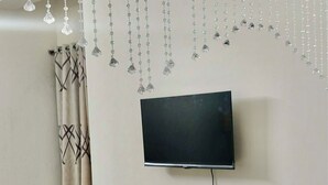 A modern living room with a flat-screen TV mounted on the wall, a dark-colored entertainment unit with drawers, and a curtain with a geometric pattern.