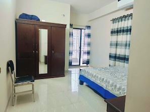 A bedroom with a wardrobe, a bed, a chair, and a window with curtains.
