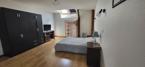 Ein Schlafzimmer mit einem Bett, einem Schreibtisch mit Computer, einem Kleiderschrank und einem Dachfenster.