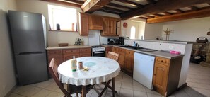 A compact kitchen with a refrigerator, stove, and dishwasher, wooden cabinets, and a dining table with chairs.