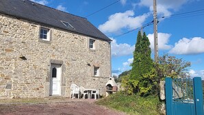 A stone building with a door, windows, and a small outdoor seating area with chairs and a table. - Gite l'écurie, in a restored farmhouse, fully equipped with pellet stove (Surtainville)