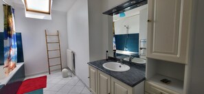 Ein Badezimmer mit einem weißen Waschbecken, einem Spiegel, einem Handtuchhalter, einer Leiter und einem Fenster.