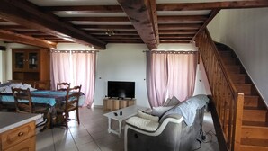 A furnished room with a bed, a TV, a sofa, a dining table, and a staircase. - Gite l'écurie, in a restored farmhouse, fully equipped with pellet stove (Surtainville)