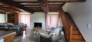 A furnished room with a bed, a TV, a sofa, a dining table, and a staircase.