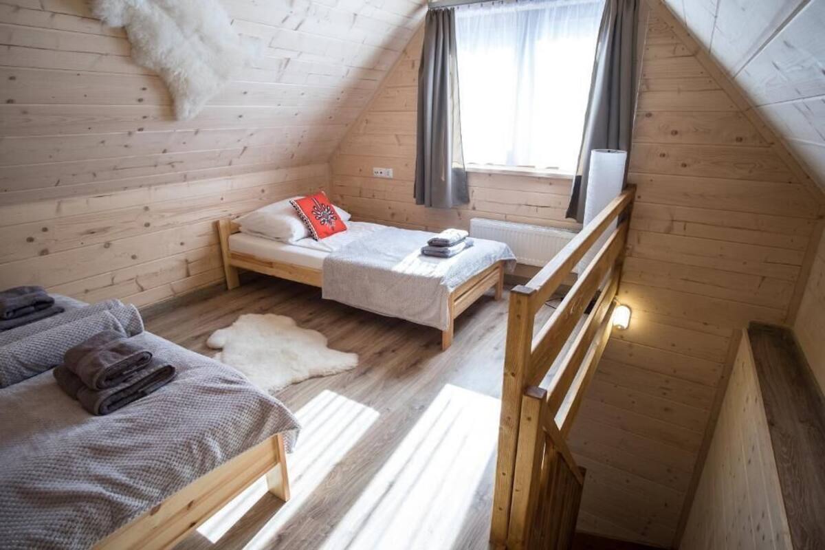 Ein kleiner, gemütlicher Raum mit zwei Holzbetten, einem Fellteppich und einem Fenster mit Vorhängen.