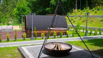 Una silla colgante con asiento tipo tazón de metal, un conjunto de columpios y un pequeño edificio con techo inclinado.