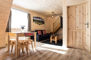 A wooden interior with a dining table, benches, a sofa, and a staircase.
