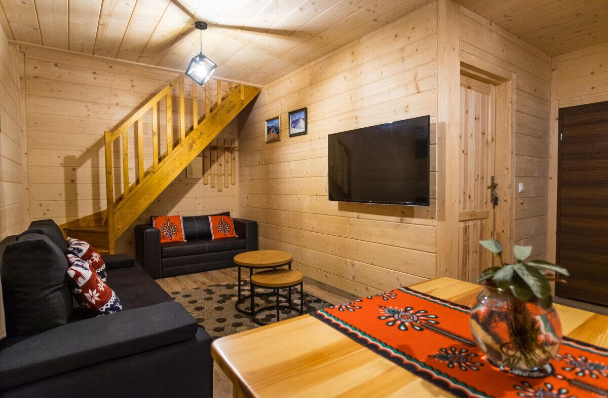 A wooden interior with a sofa, a small round table, a TV, and a staircase.