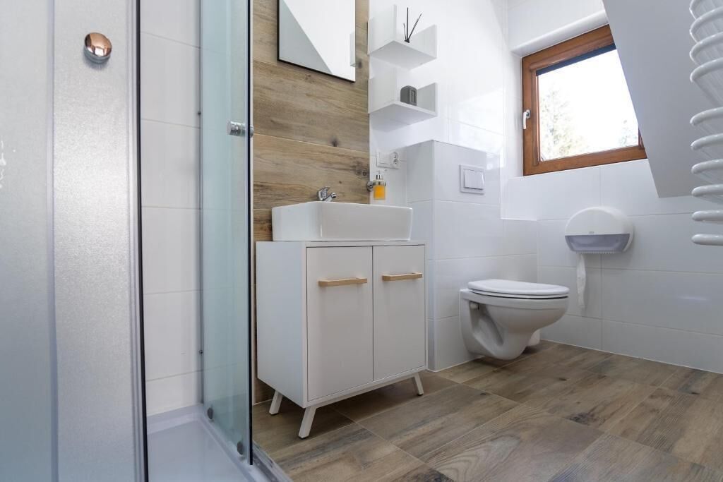 Un baño moderno con cabina de ducha de vidrio, un tocador blanco y una pared de acento de madera, y un inodoro.