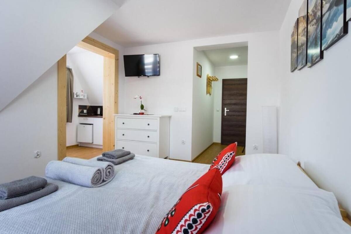 Ein Schlafzimmer mit Bett, Fernseher, einer kleinen Küchenzeile und einer Tür zu einem weiteren Raum.