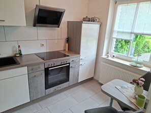 Una cucina moderna con piano cottura, forno e microonde integrati, una finestra vista su spazi verdi, e un'area pranzo con tavolo e sedia.