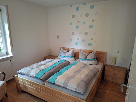 A neatly made bed with striped bedding, a wooden headboard, and a bedside table with a lamp.. Vacation apartment in Marsberg (Sauerland) with terrace directly on the Diemel cycle path