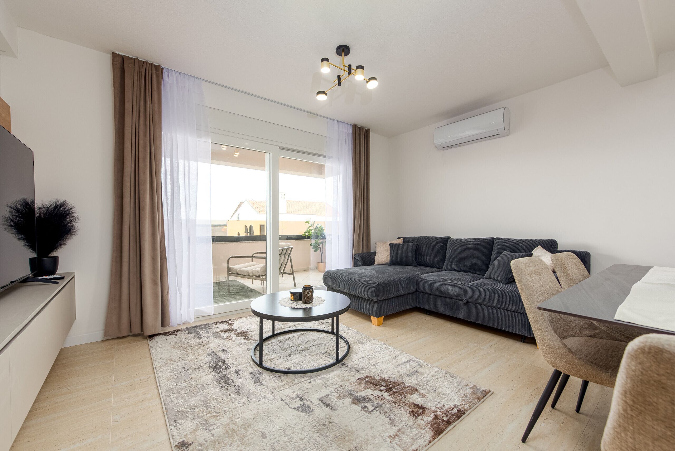 Un salon moderne comprenant un canapé, une table à manger, une table basse et une vue sur un balcon extérieur, accessible par une porte vitrée.