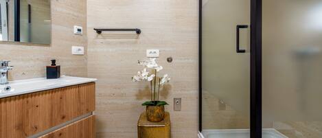 A modern bathroom with a wooden vanity, a glass shower enclosure, and a vase with white flowers.