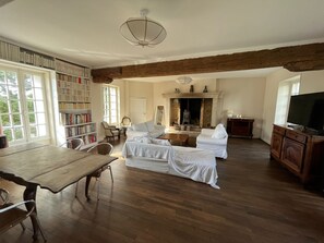 Ein geräumiges Wohnzimmer mit Holzboden, Kamin, Fernseher und Bücherregal.