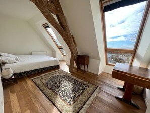 Ein Schlafzimmer mit Bett, Holzboden, Teppich, Schreibtisch und Fenster mit Blick.