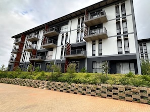 A multi-story building with balconies, a brick pathway, and greenery. - Mayamuye Lifestyles 3-bedroom (Mbombela)