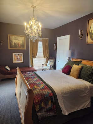 A bedroom with a large bed, a chandelier, a chair, and a door. - The Thornton House Bed and Breakfast (Lansing)