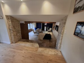 Ein großzügiges Loft mit freiliegenden Steinwänden, einer Holztreppe und einer gemütlichen Sitzecke mit Sofa und Sesseln.