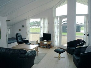 A living room with a TV, leather chairs, a wooden table, and large windows. - 4 Star Holiday Home in Rudkobing (Rudkobing)