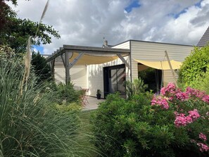 Ein überdachter Außenbereich mit Terrasse, einer Holz-Pergola und Kübelpflanzen.
