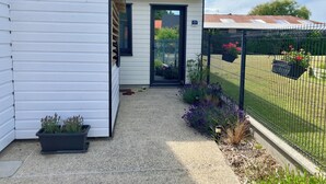 Une maison à l’extérieur blanc, avec une porte noire et un petit jardin agrémenté de plantes et d’une clôture.
