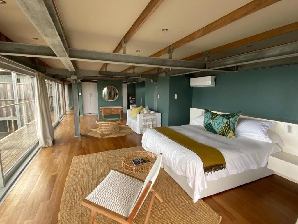 A bedroom with a large bed, a bedside table, a chair, a window, and a mirror.