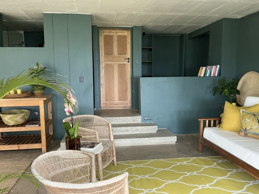 Une pièce comprenant un lit, une table en bois, des chaises en osier, une plante en pot et un escalier menant à une autre pièce.