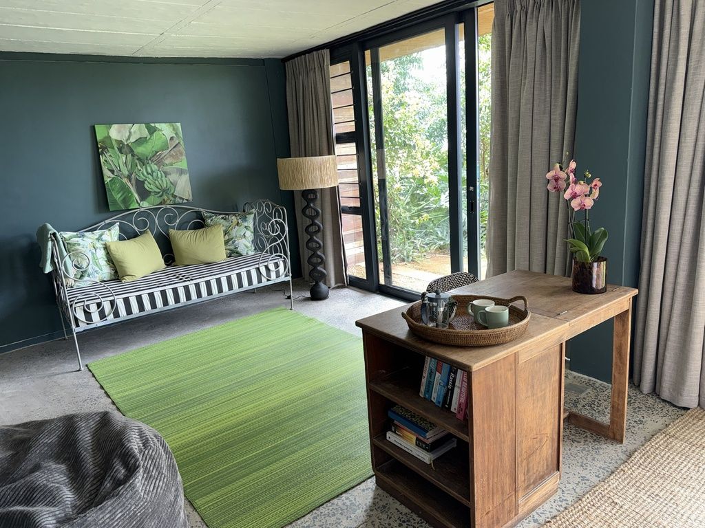 Una habitación con un sofá, una mesita de madera, un tapete verde y un ventanal con cortinas.