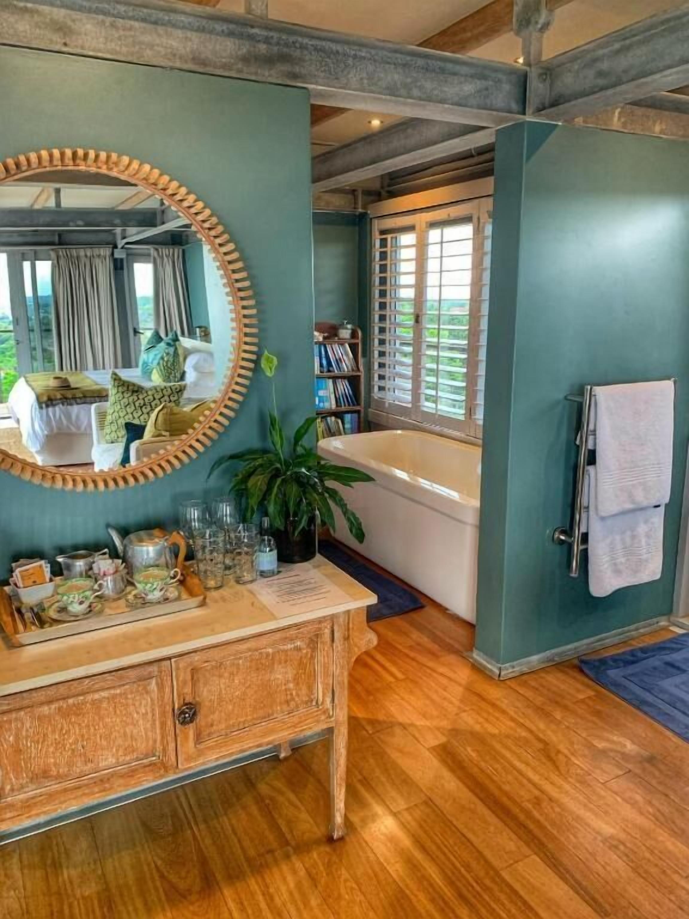 Een badkamer met een bad, een wastafel met spiegel en een raam met gordijnen.