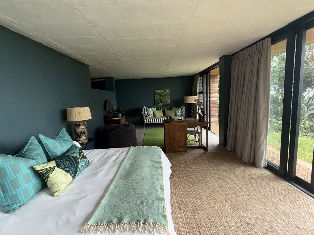 Un dormitorio con cama, escritorio y vista al verde exterior.