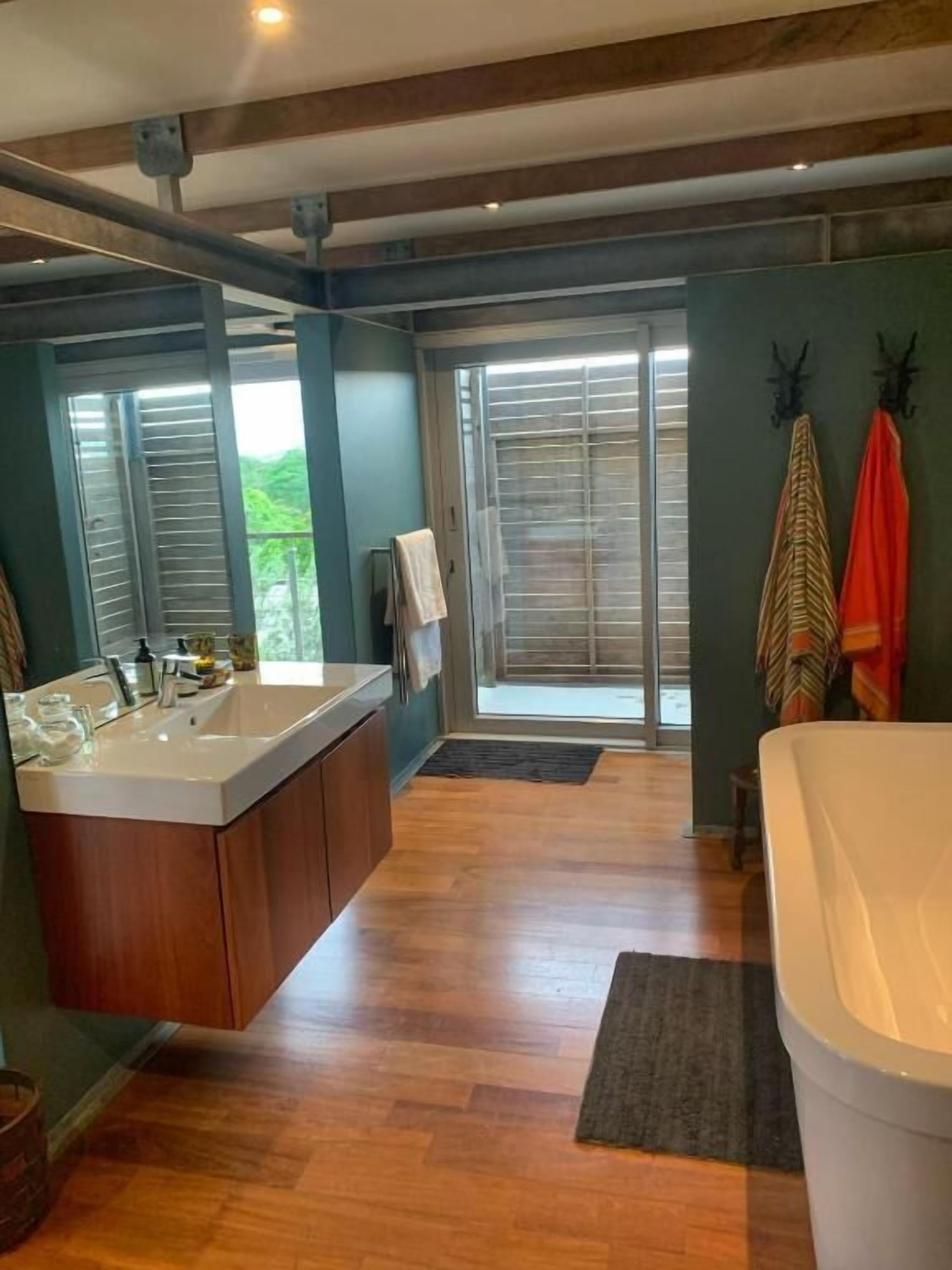 A bathroom with a large bathtub, a sink with a wooden vanity, and a window with blinds.