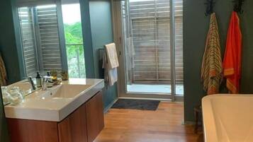 A bathroom with a large bathtub, a sink with a wooden vanity, and a window with blinds.
