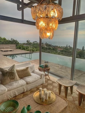 A modern interior with a sofa, a round table with candles, and a view of a pool and landscape.