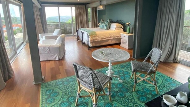 A hotel room with a bed, a sitting area with a table and chairs, and a view through large windows. - The Seaglass (Durban)