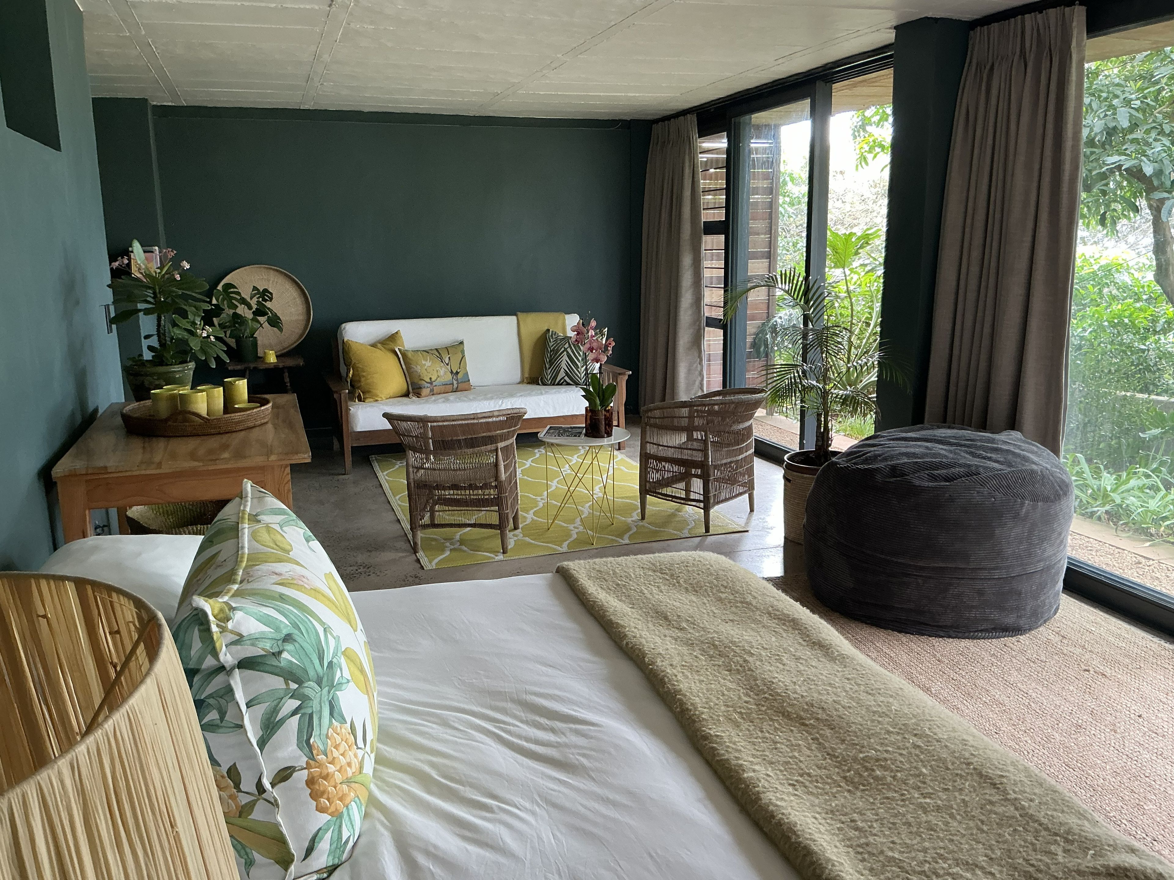 A room with a bed, a sofa, a dining table with candles, and a large window with curtains.
