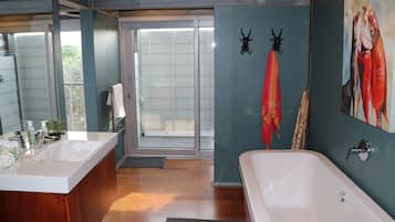 A bathroom with a bathtub, a sink, and a mirror. There is a door leading to an outdoor area.