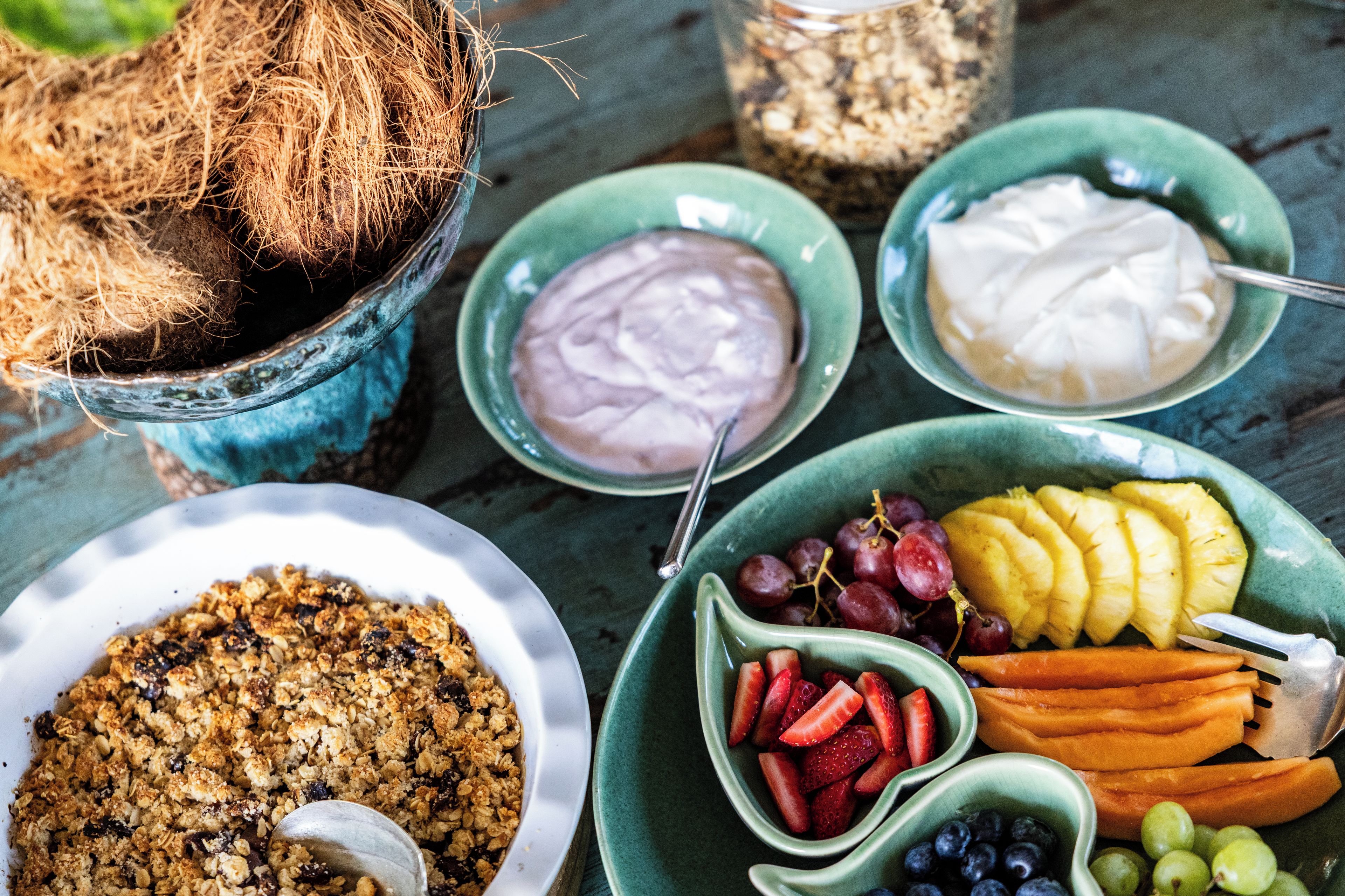 Taula amb diversos aliments, incloent un bol de granola, fruita fresca i dos bols de iogurt.